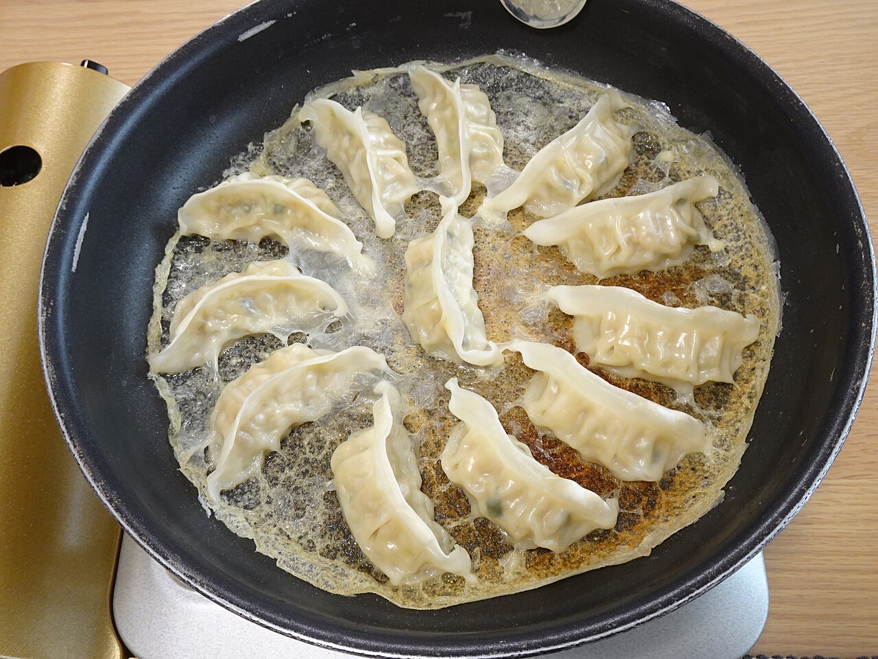 Gyoza dumplings in a frying pan, illustrative of one possible package-authorized cooking method