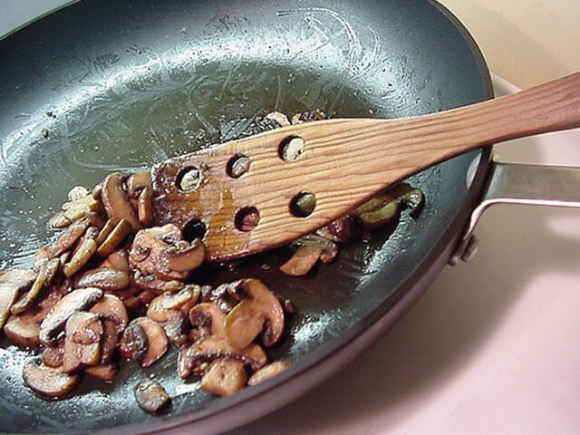 Baby bella mushrooms sautéing in a skillet with a wooden spatula